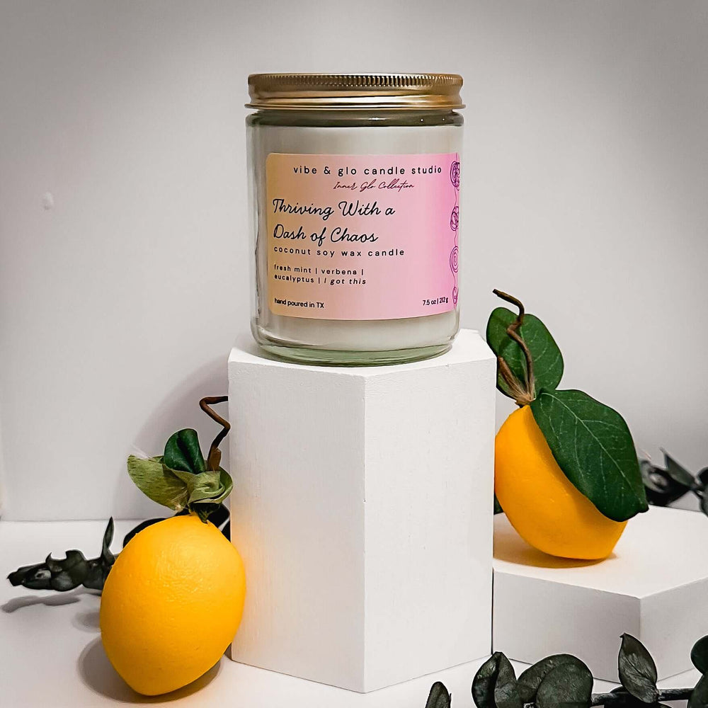 Thriving With a Dash of Chaos coconut soy wax candle with fresh mint, verbena, and eucalyptus. Styled with lemons on a clean white background for a bright, energizing feel.
