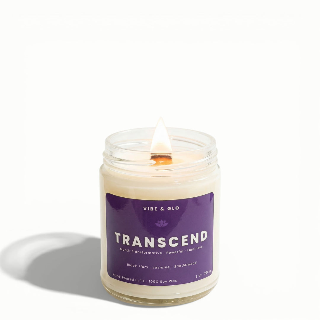 Transcend black plum, jasmine, and sandalwood soy candle by Vibe & Glo with lit wooden wick in clear glass jar.