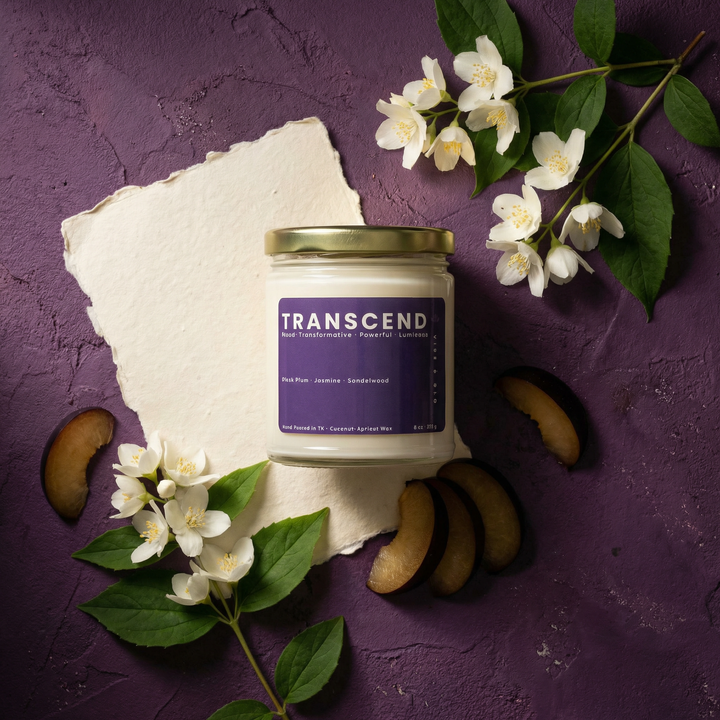 Transcend candle with black plum, jasmine, and sandalwood notes styled with fresh white florals and sliced plum on a textured purple background