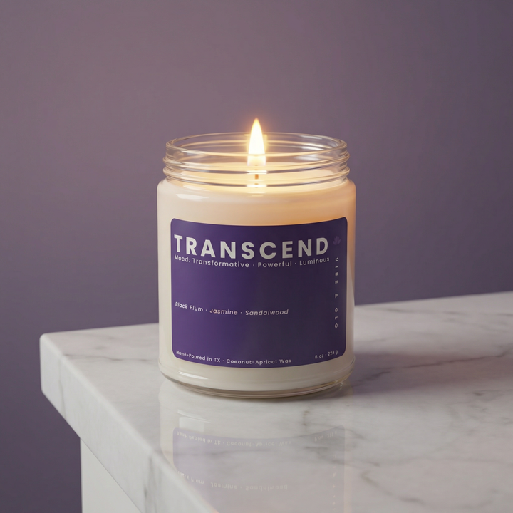 Transcend scented candle in clear glass jar lit on marble surface, clean coconut apricot wax candle with black plum jasmine sandalwood fragrance