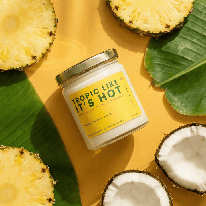 Tropic Like It’s Hot tropical fruit candle styled with pineapple and coconut on a bright yellow background