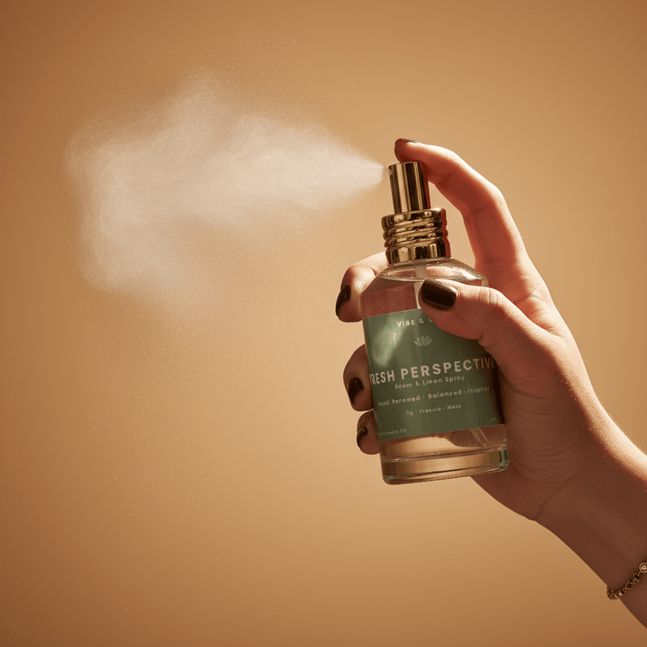 Hand spraying Vibe & Glo Fresh Perspective room and linen spray, mist dispersing against a warm neutral background for a fresh, balanced home fragrance moment.