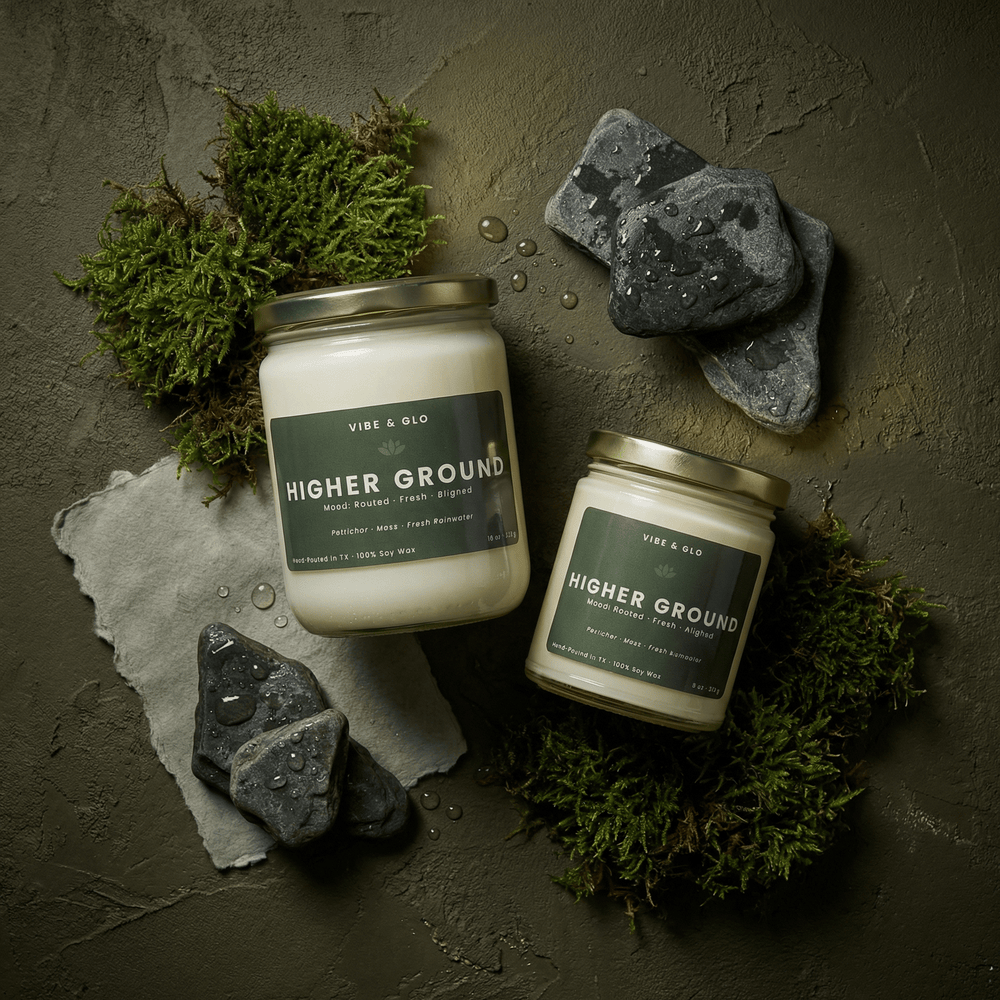 Higher Ground soy candles in 16 oz and 8 oz glass jars with gold lids, styled with moss, wet stones, and water droplets to reflect petrichor and fresh rainwater notes.