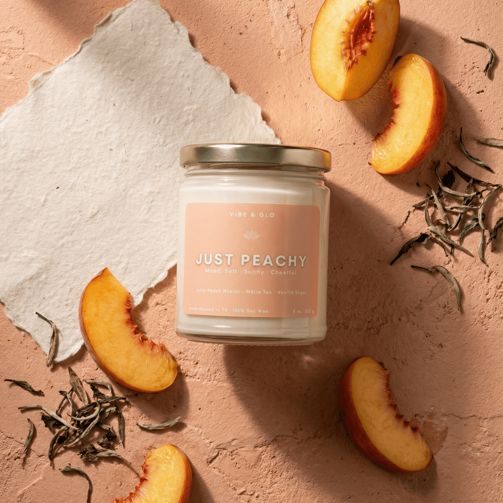 Just Peachy 8 oz soy candle featuring peach nectar, white tea, and vanilla sugar surrounded by peach slices and dried tea leaves in a bright flatlay.