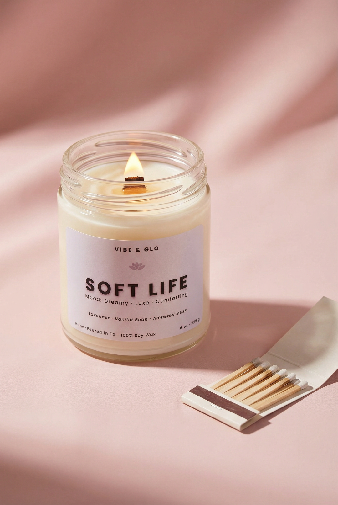 Soft Life soy candle by Vibe & Glo glowing on a pink background with matches for a dreamy self-care ritual