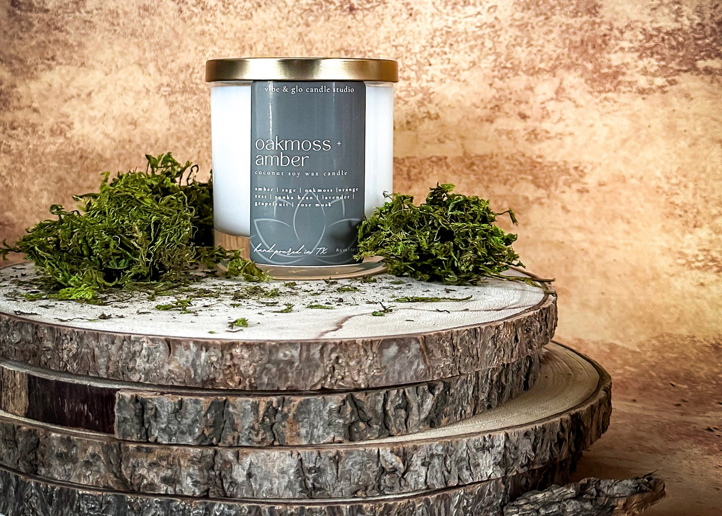 Candle labeled 'Oakmoss & Amber' on a wooden surface with greenery