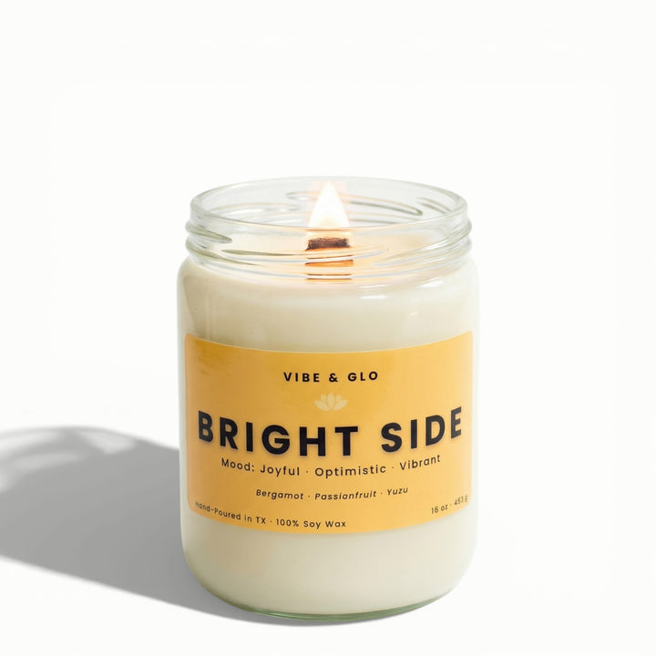 Bright Side 16 oz wooden wick soy candle by Vibe & Glo with bergamot, passionfruit, and yuzu, lit wooden wick in clear glass jar, front-facing high-key studio photograph.