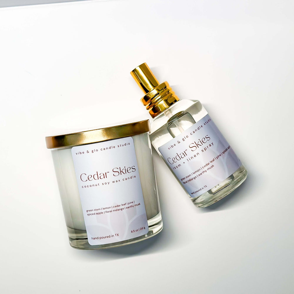 Candle and spray bottle labeled 'Cedar Skies' on a white background