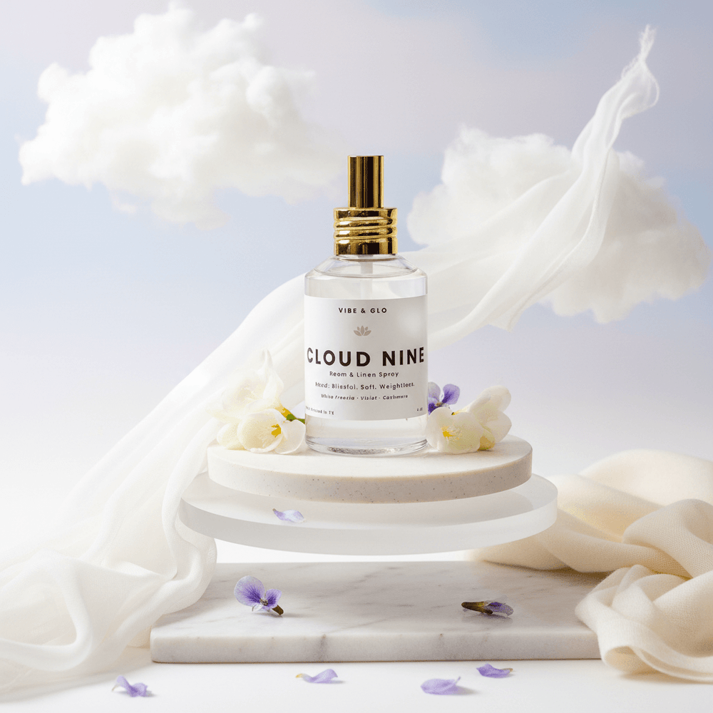 Cloud Nine room and linen spray bottle on a marble stand with white fabric and flowers in the background