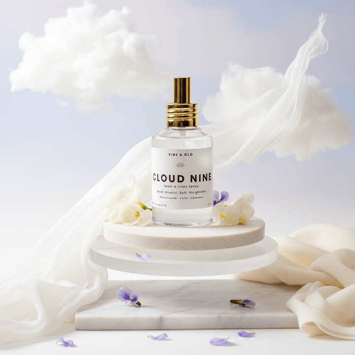 Cloud Nine room and linen spray bottle on a marble stand with white fabric and flowers in the background