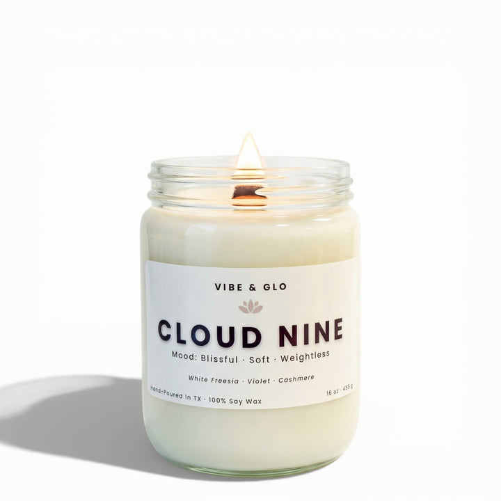 Cloud Nine 16 oz wooden wick soy candle by Vibe & Glo with white freesia, violet, and cashmere in a clear glass jar, lit wooden wick, front-facing studio product photo on white background.