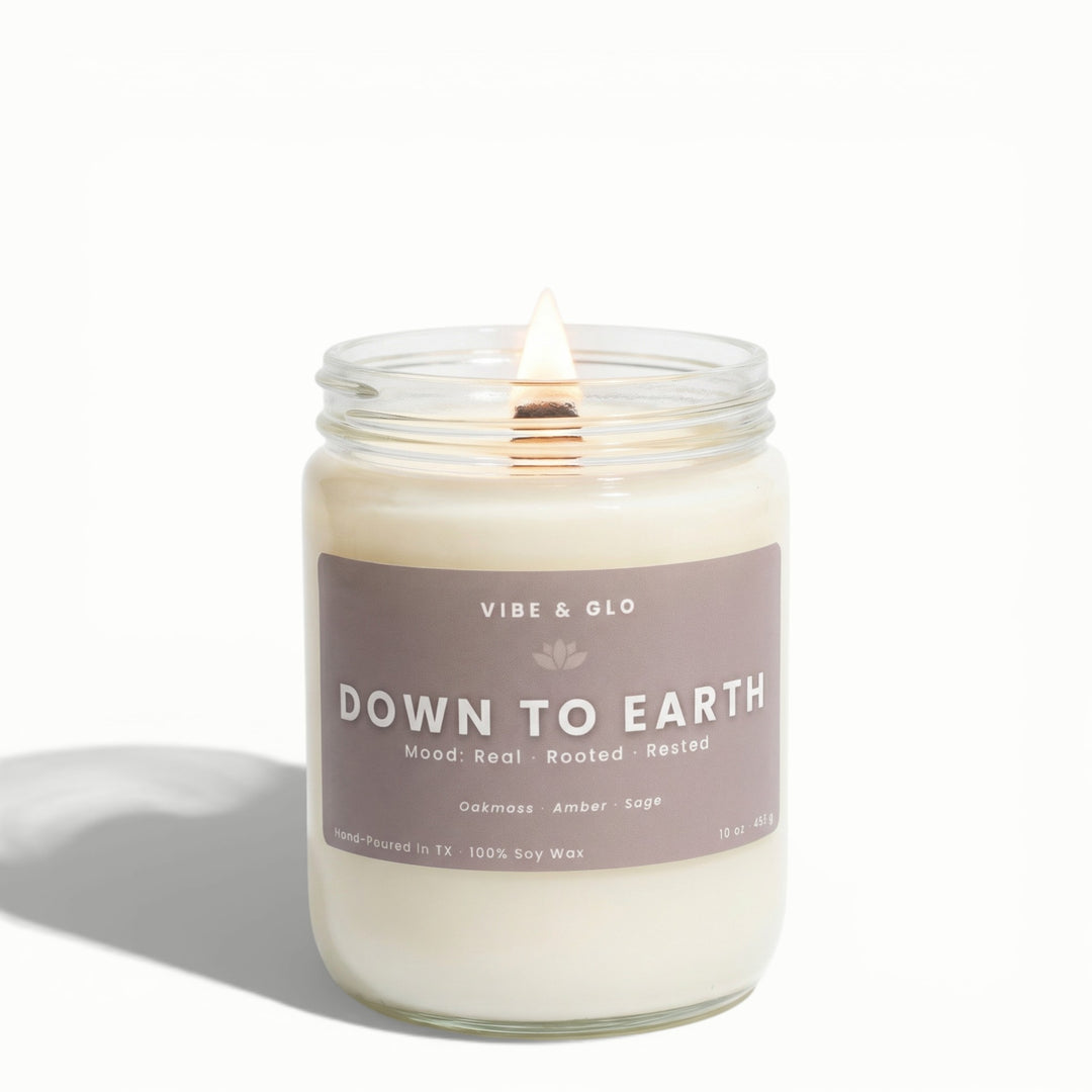 Down to Earth 16 oz wooden wick soy candle by Vibe & Glo with oakmoss, amber, and sage, lit wooden wick in clear glass jar, minimal white background product image.