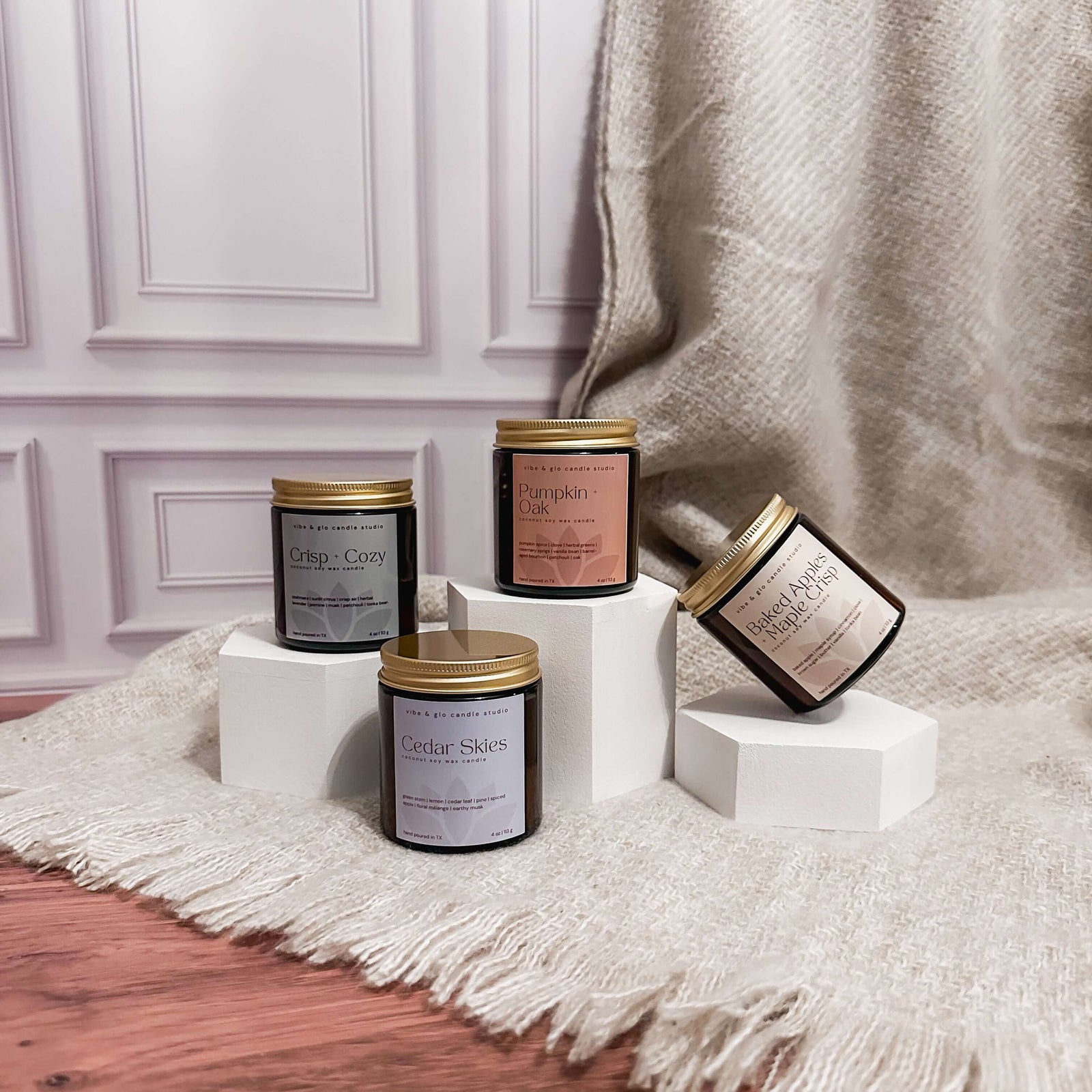 Four candles with gold lids on white stands against a neutral background