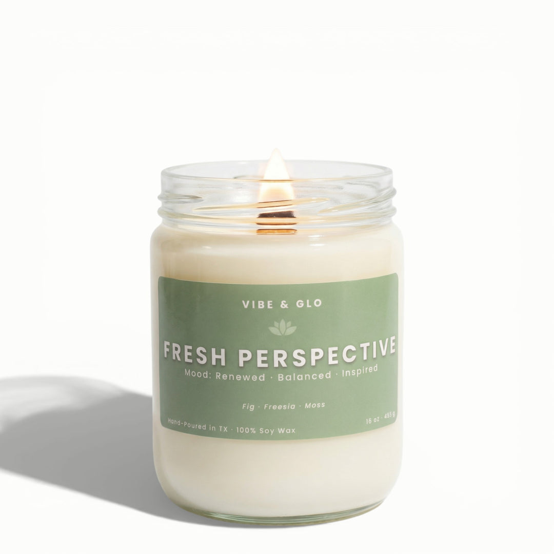 Fresh Perspective 16 oz wooden wick soy candle by Vibe & Glo with fig, freesia, and moss, lit wooden wick in clear glass jar, high-key studio product photography on white background.