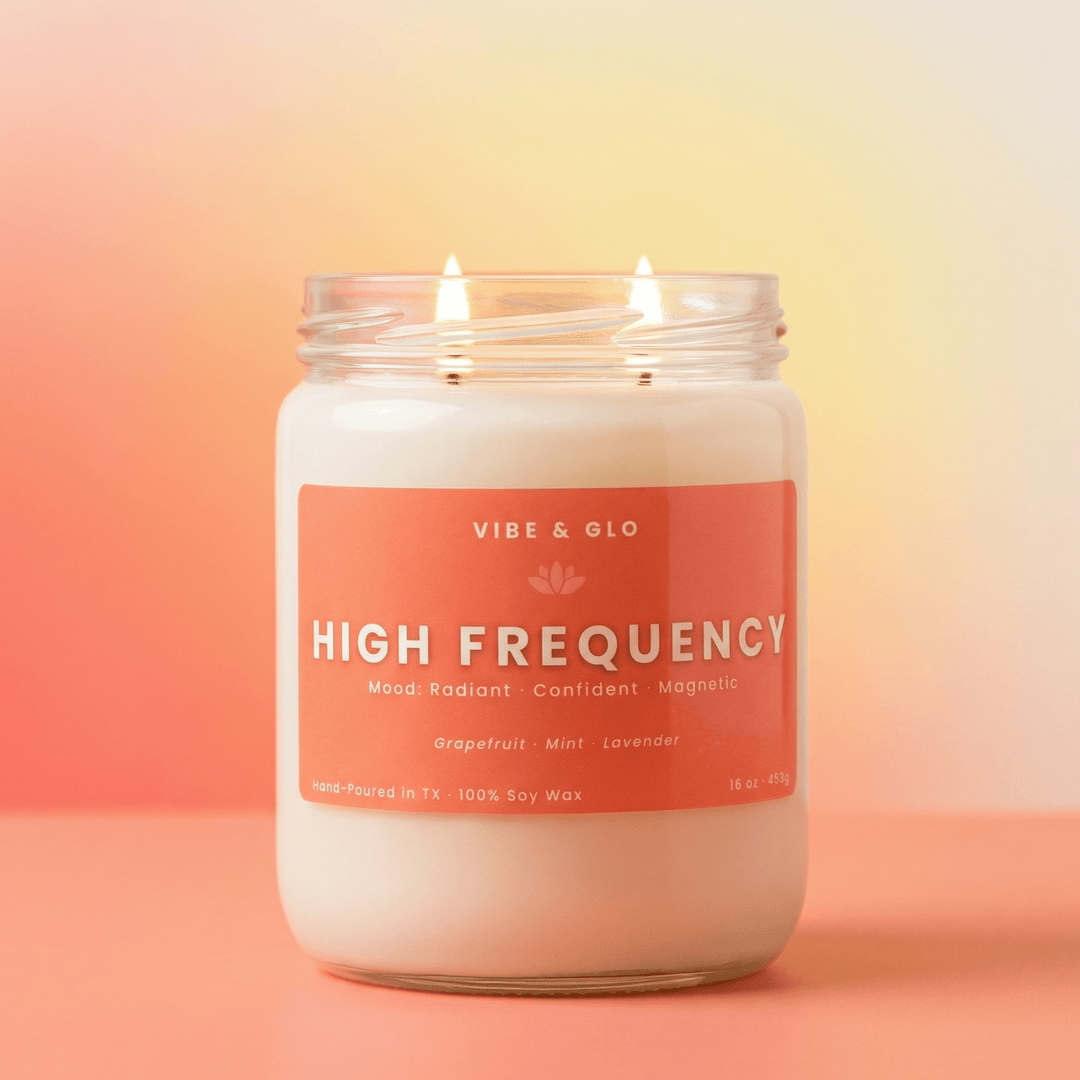 Close-up of a lit High Frequency 2-wick soy candle by Vibe & Glo against a soft coral gradient background, showcasing a clean, modern candle designed for a bright and energizing atmosphere.