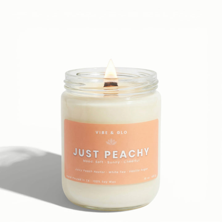 Just Peachy 16 oz wooden wick soy candle by Vibe & Glo with juicy peach nectar, white tea, and vanilla sugar, lit wooden wick, clean white background product photo.