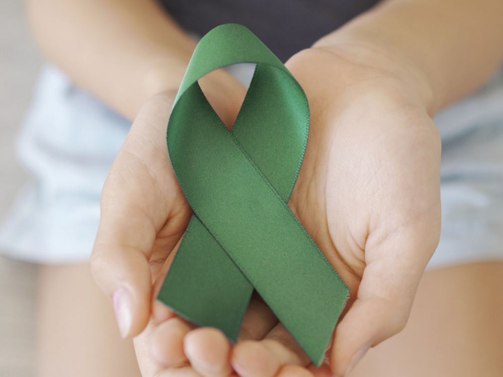 Hands holding green mental health awareness ribbon symbolizing hope and emotional wellness.