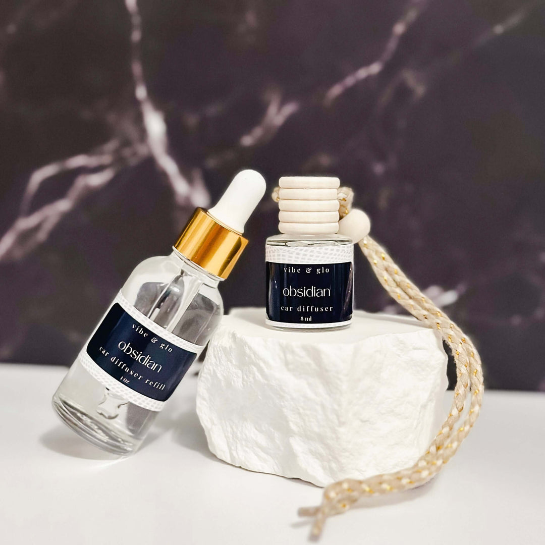 Vibe & Glo 1 oz car diffuser refill bottle with hanging diffuser on a stone surface.