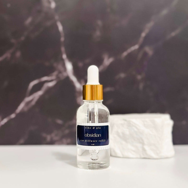 1 oz car diffuser refill bottle with dropper, obsidian scent, against a dark marble background.