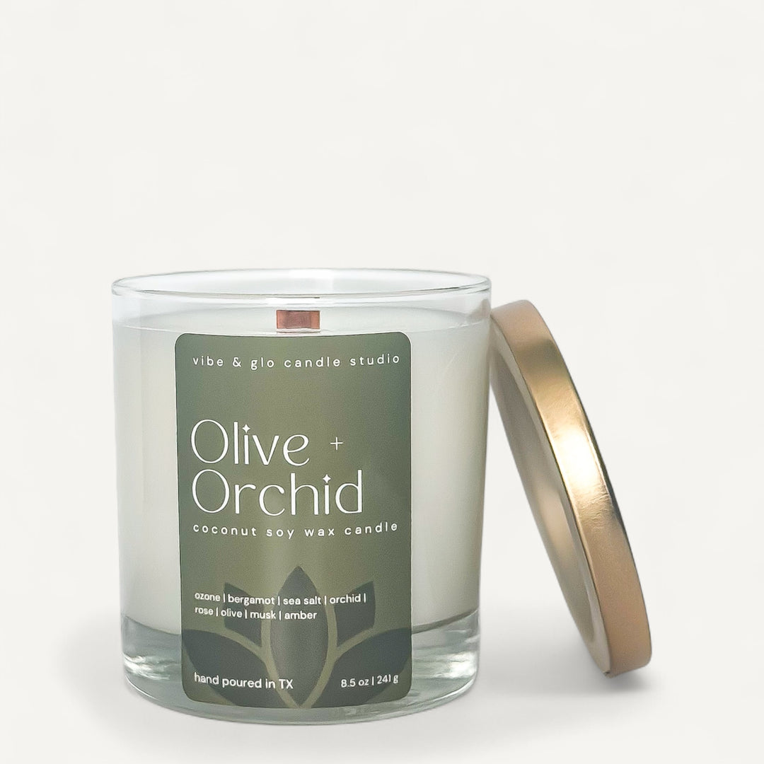 Olive + Orchid coconut soy wax candle in glass jar with gold lid, featuring citrus and floral scents for a spa-inspired experience.