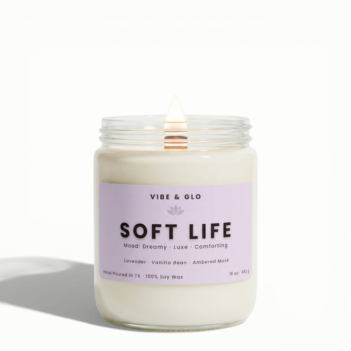 Soft Life 16 oz wooden wick soy candle by Vibe & Glo with lavender, vanilla bean, and ambered musk, lit wooden wick in clear glass jar, front-facing product image.