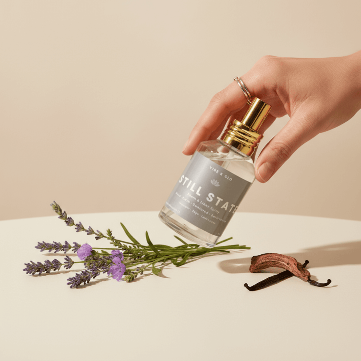 Hand holding a bottle labeled 'Still State' with lavender and vanilla beans on a beige background