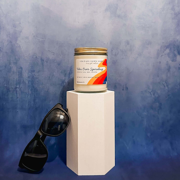 Vibes Over Spiraling coconut soy wax candle with sunglasses against a blue textured background.