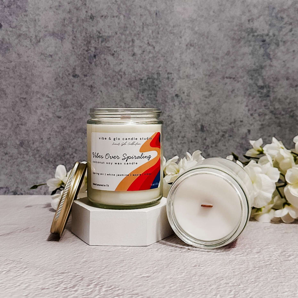 Vibes Over Spiraling coconut soy wax candle with white flowers on a grey background.