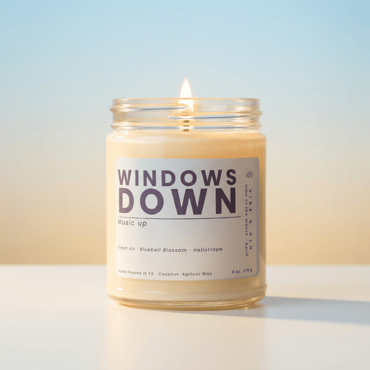 Windows Down April 2026 candle of the month by Vibe & Glo burning with a soft glow, clean coconut apricot wax candle in glass jar with minimalist label